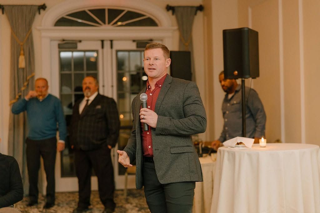 Steven Hauck addressing an audience at an elegant indoor venue, holding a microphone