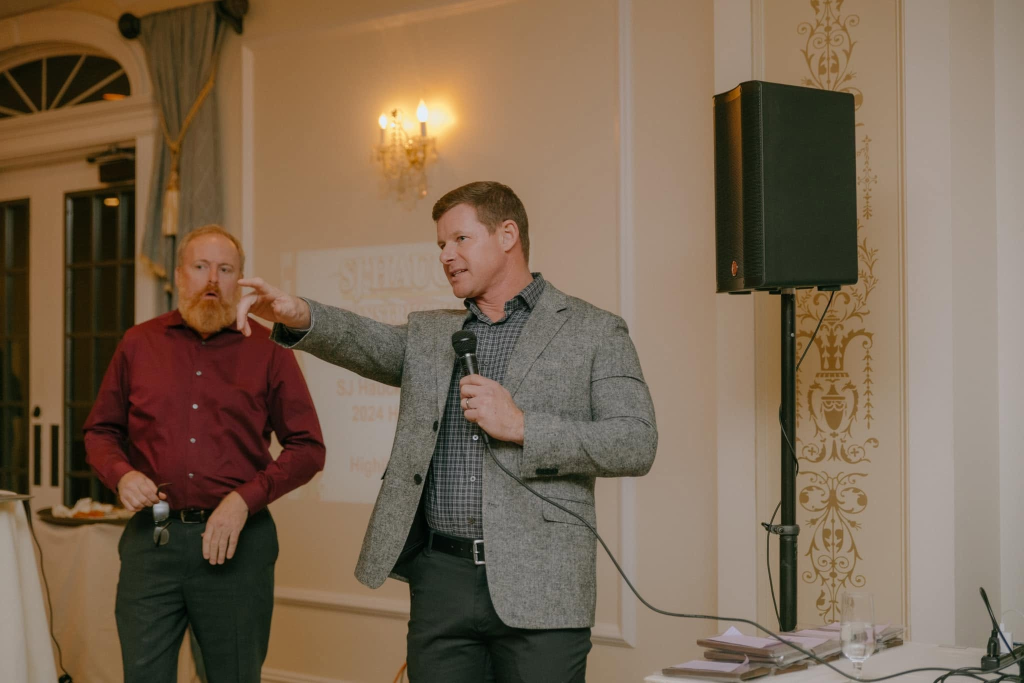 Steven Hauck speaking at an industry event, holding a microphone and gesturing to the audience